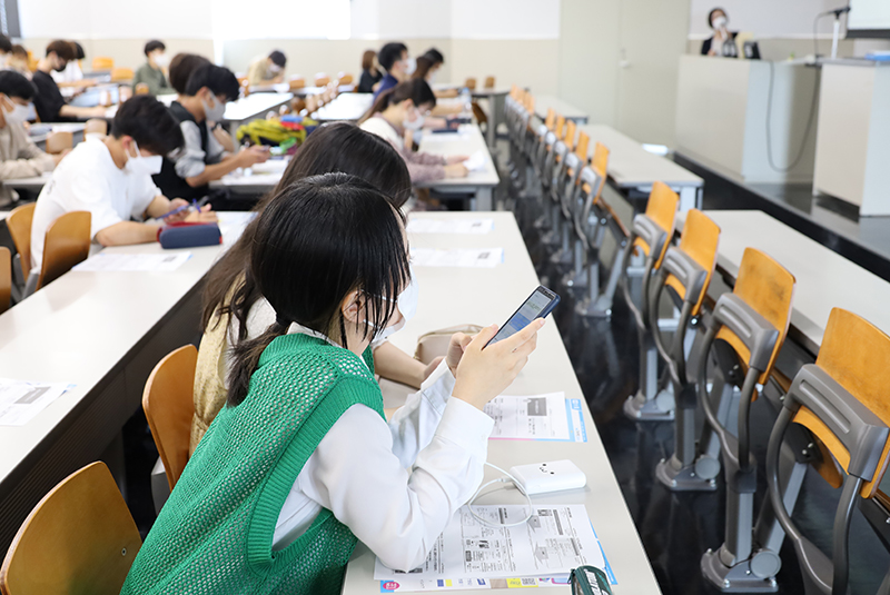 スマホを使い、説明を受ける学生たち